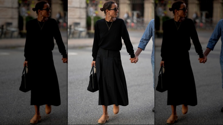 A woman wearing a black crew sweater tucked into a skirt with mules