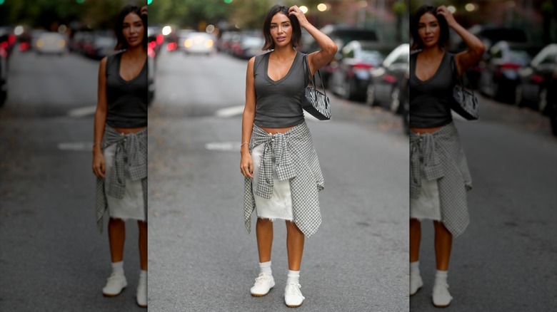 A woman wearing a skirt and tank with white sneakers and socks