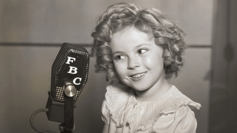 Young Shirley Temple looking into a microphone in the 1930s