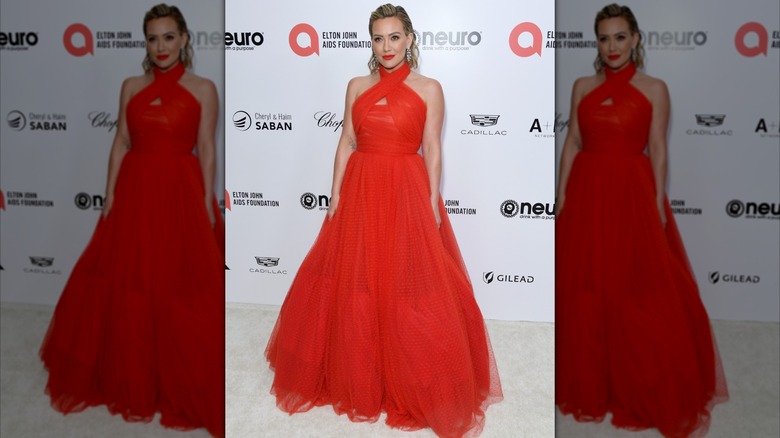 Hilary Duff with her hair slicked back posing at an event wearing a bright red dress with a full skirt.