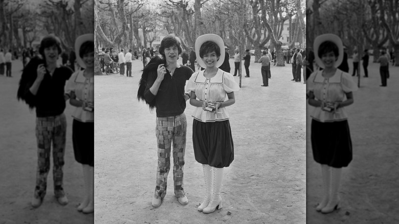 Mick Jagger wearing madras pants and a polo shirt posing with wife Bianca Jagger wearing an old-timey outfit.