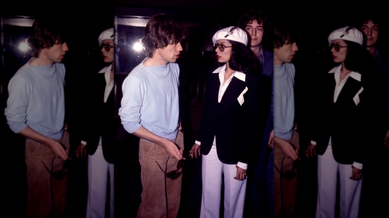 Mick Jagger in a blue sweatshirt and corduroy pants pictured next to wife Bianca Jagger wearing a black blazer and white cap.