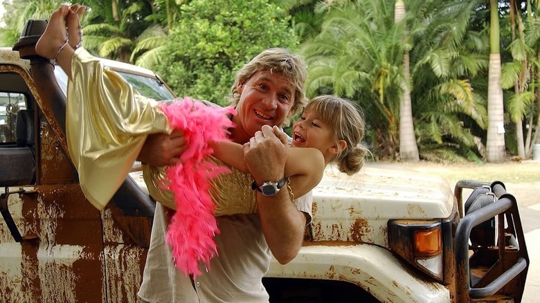 Steve Irwin holding Bindi Irwin, who's dressed up with a pink feather boa