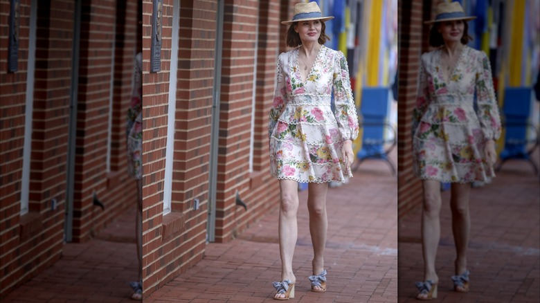 Geena Davis wearing a white dress with flowers and a straw hat while walking
