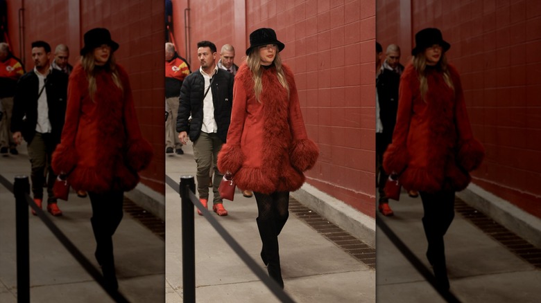 Taylor Swift walking in a red fur-trimmed coat and boots