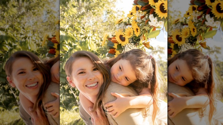 Bindi Irwin cuddling with her daughter Grace below a sunflower garland