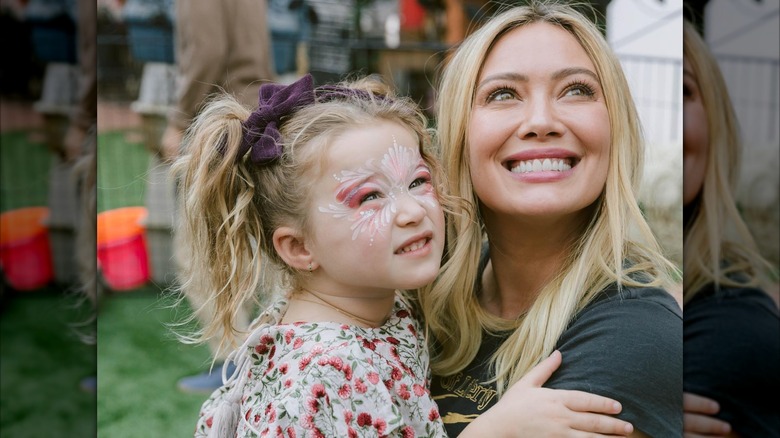 Hilary Duff wears her blond hair straight down while smiling and holding her daughter Banks at her third birthday party.
