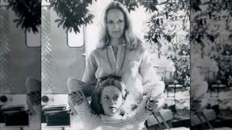 A black-and-white photo shows a young Melanie Griffith sitting in a chair while her mother Tippi Hedren hugs her from behind