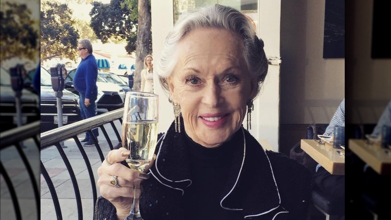 Tippi Hedren wears a black jacket and holds up a glass of champagne while dining at a restaurant