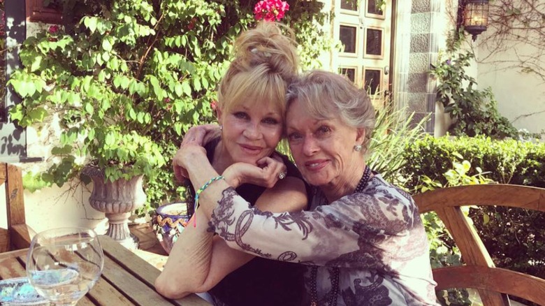 Melanie Griffith and Tippi Hedren embrace each other while posing for a photo outdoors at a picnic table