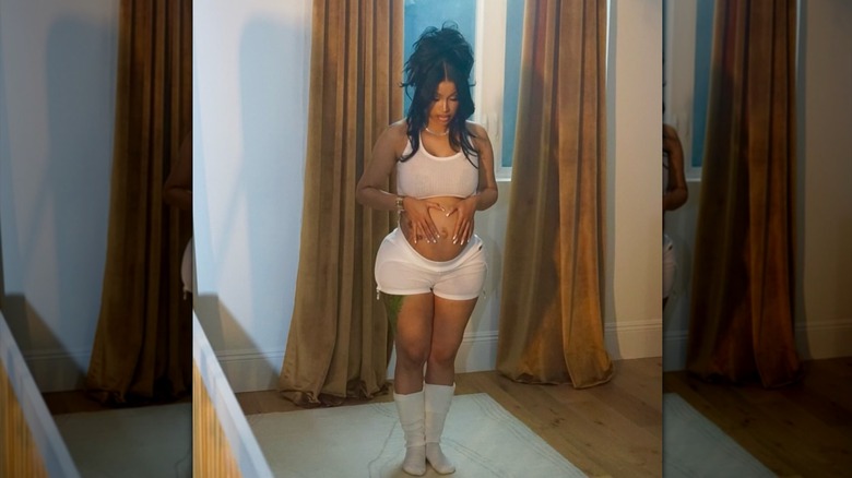 Cardi B holding her baby bump while in a white two piece