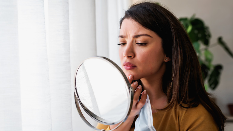 woman looking blemish in mirror