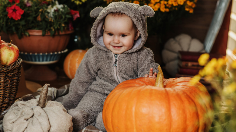 A baby in a bear costume next to a pumpkin