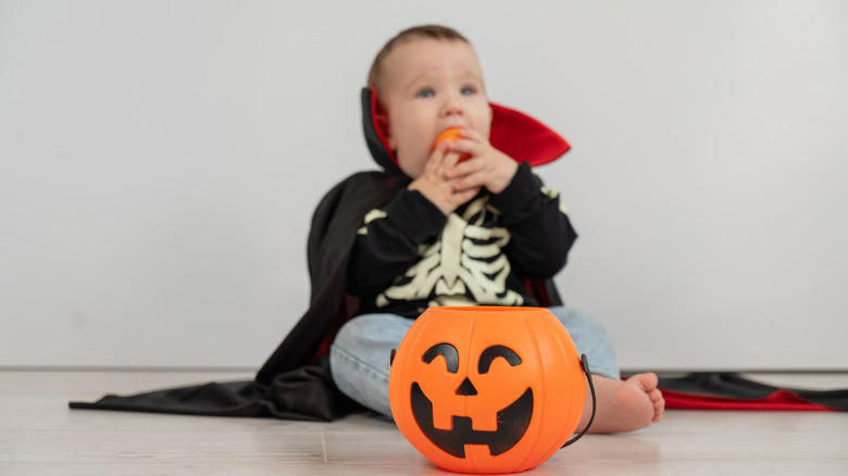 A baby in a vampire costume and pumpkin decor.