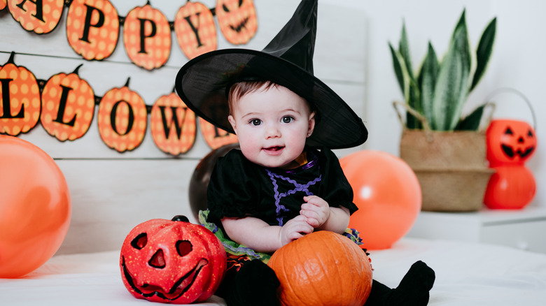 A baby in a witch costume with pumpkin decor.