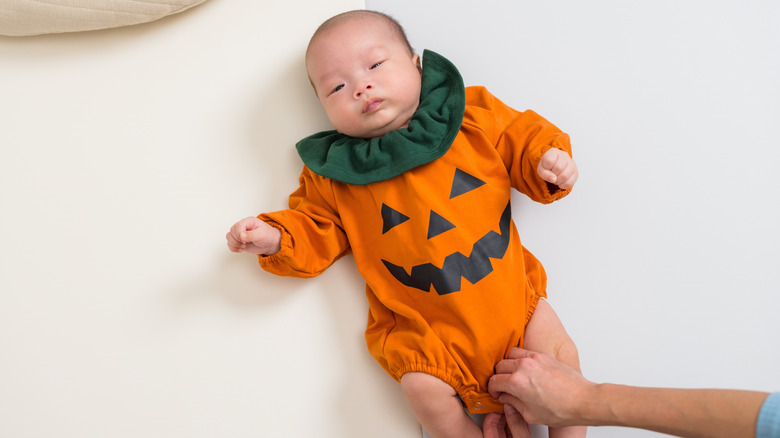 A baby in a jack-o-lantern romper.