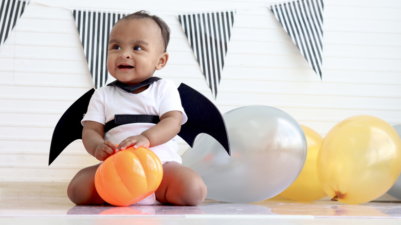 A baby in a bat costume playing with a pumpkin toy.