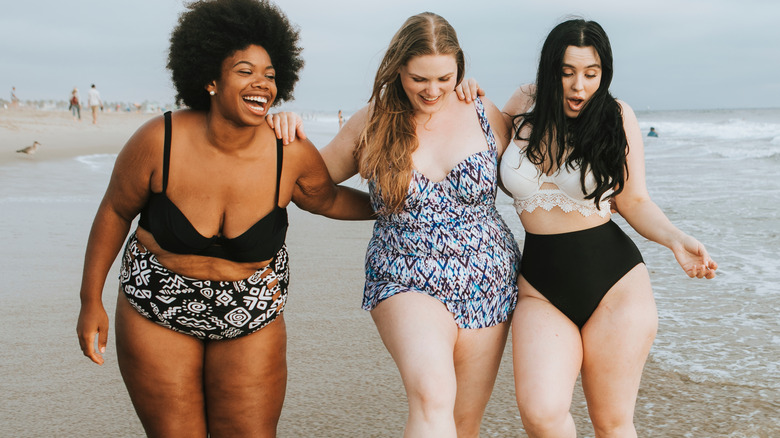 Three women at the beach all wearing different swimsuits
