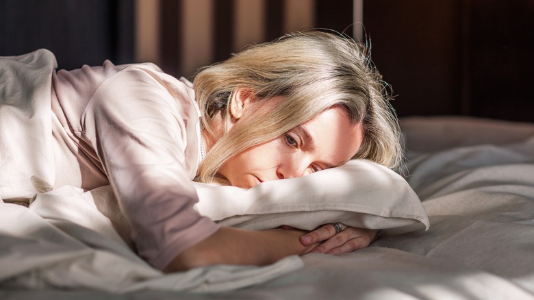 sad woman laying on bed hugging pillow