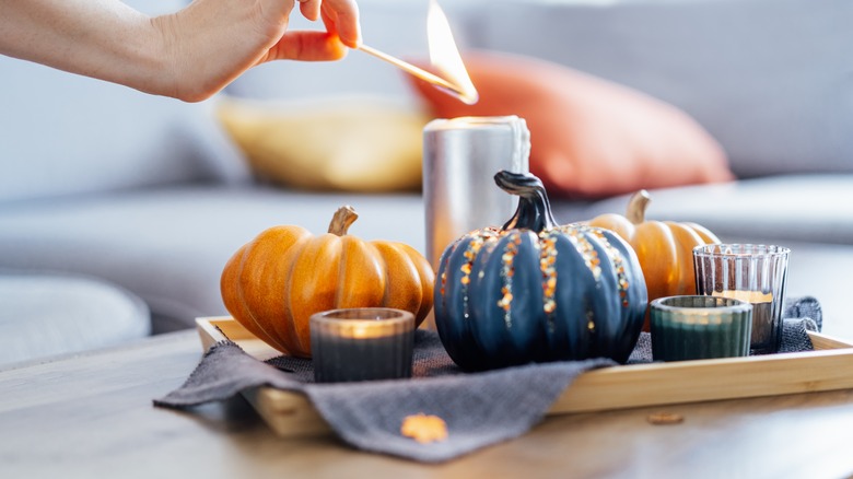 hand reaching out to light a candle on a tray of mini pumpkins