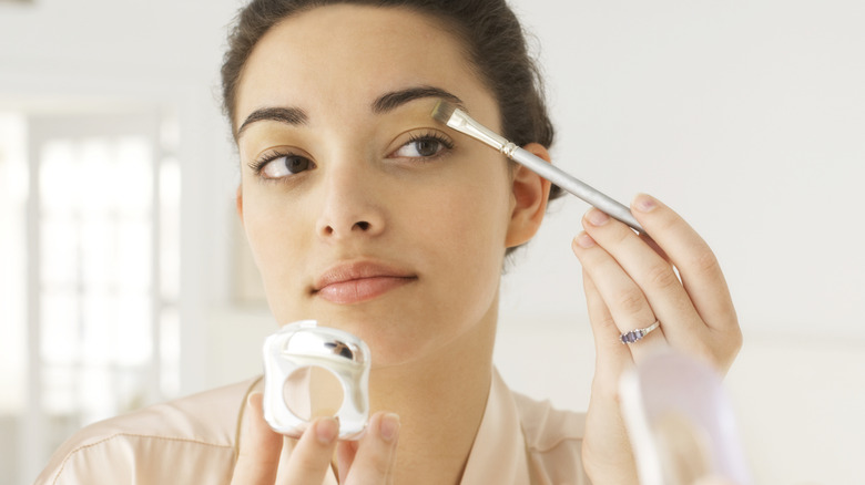 Woman applying makeup in mirror