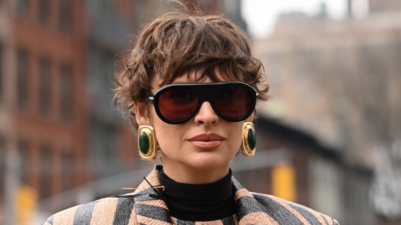 A woman wearing sunglasses, big earrings, and her hair in a wavy pixie cut
