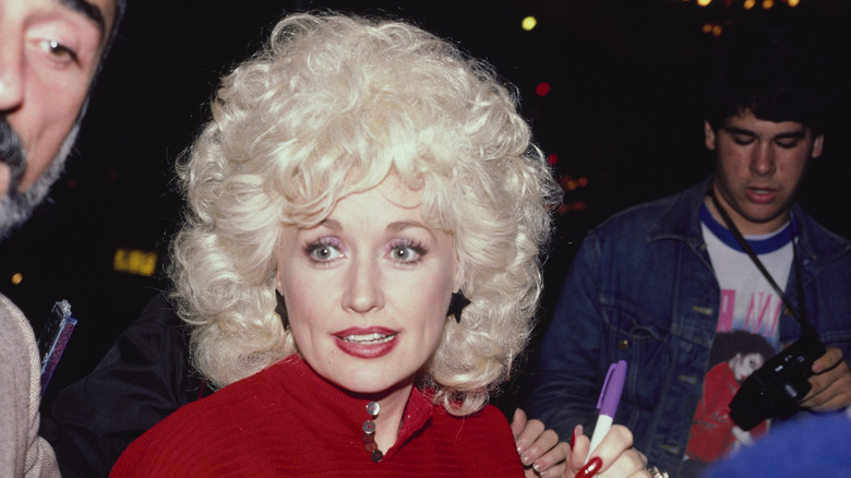 Dolly Parton signing autographs in 1984 wearing a red top with star-shaped earrings.