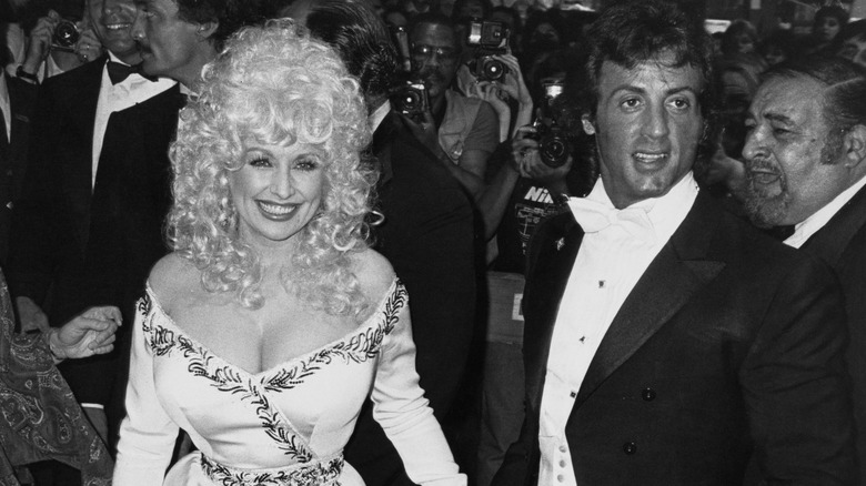 Dolly Parton in 1984 at the premiere of "Rhinestone" wearing a white dress posing with Sylvester Stallone.
