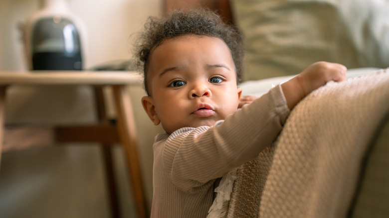 A baby standing up against a couch