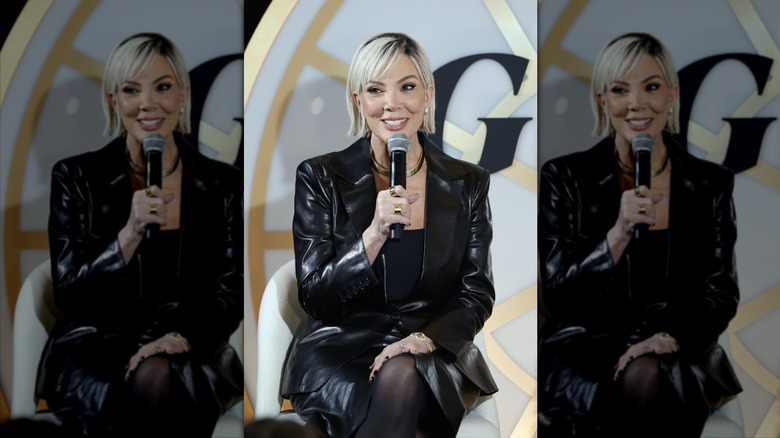 Kris Jenner smiles behind a microphone with a blond bob