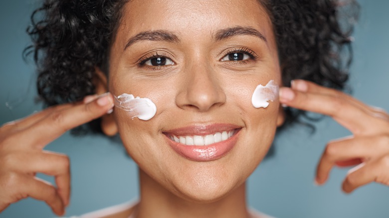 smiling woman applying cream on cheeks