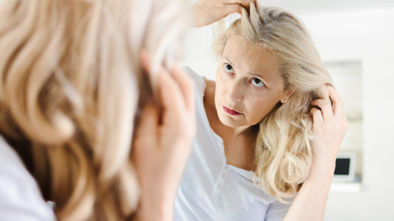 A woman with gray hair insecting her hair in the mirror