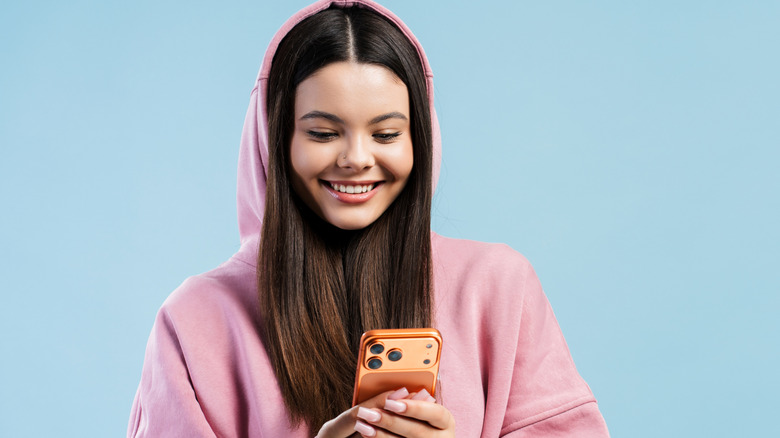 A girl wearing a hoodie and holding a smartphone