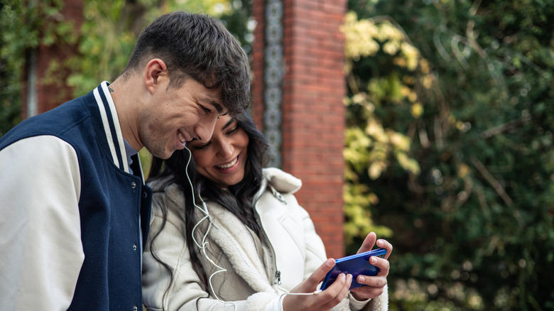 A couple wearing headphones and laughing at a smartphone screen