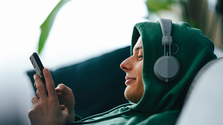 A young man wearing headphones and typing on his smartphone