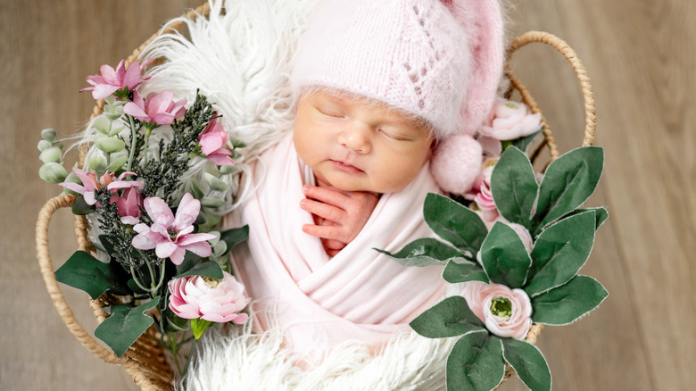 A baby girl sleeping in a basket of flowers