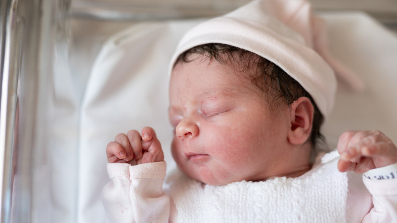 A newborn baby wearing a pink cap in a cradle