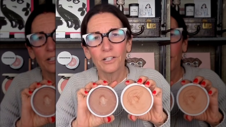 Bobbi Brown wearing glasses holding one of her brand's products, Miracle Balm.