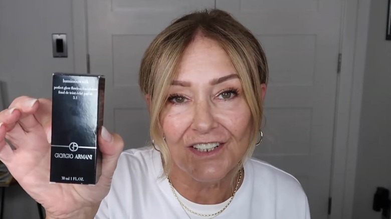 Woman wearing a white T-short holding up a container of Giorgio Armani Luminous Silk Foundation.