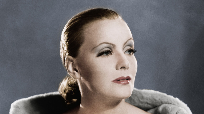 Greta Garbo pictured wearing a low chignon posing against a gray backdrop.