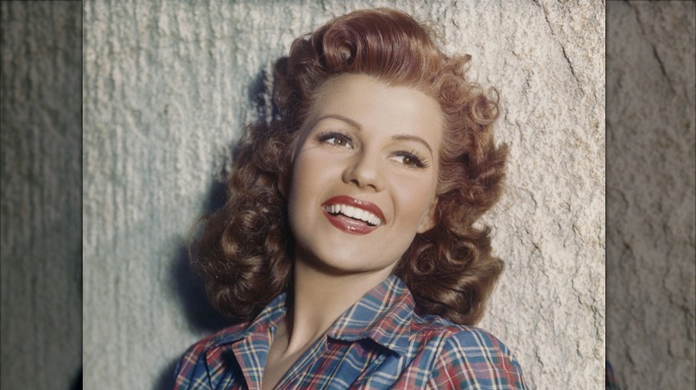 Rita Hayworth smiling in a plaid shirt with curly red hair.