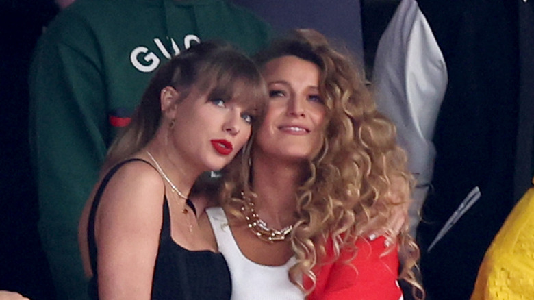 Taylor Swift in a black outfit with red lips and Blake Lively in a white shirt with very curly hair at the Super Bowl.