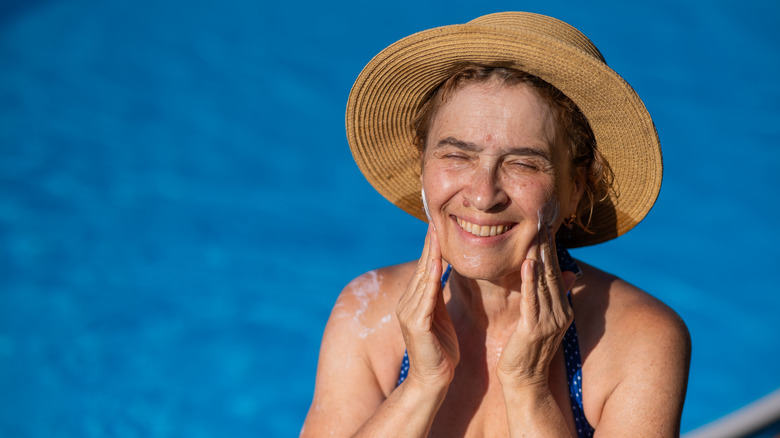 An older woman applying sunscreen while by a pool