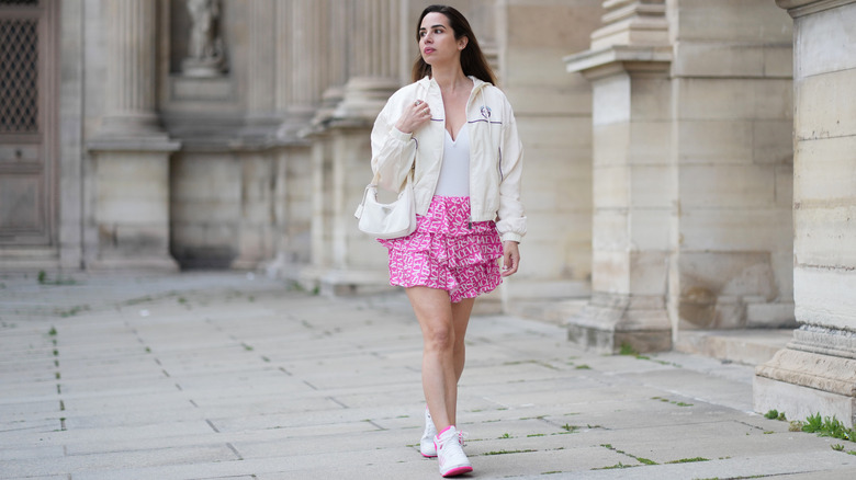 A person wearing a pink flouncy skirt with a beige sports jacket