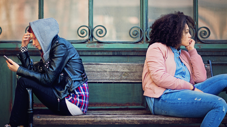 Angry friends sit on opposite ends of a bench