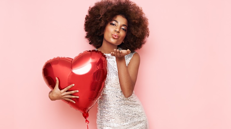 Woman holding a heart shaped balloon and blowing a kiss