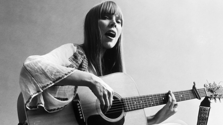 A portrait of Joni Mitchell sitting on the floor playing guitar