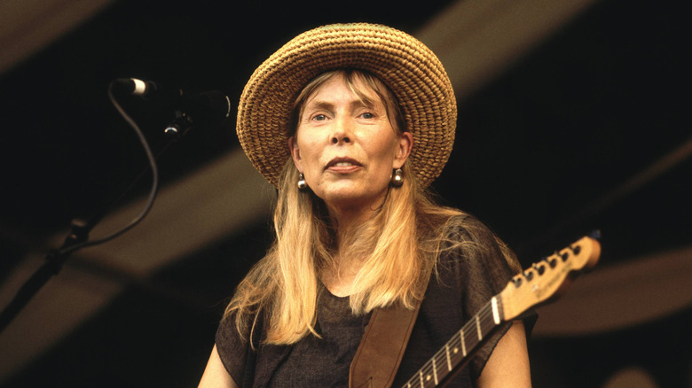 Joni Mitchell performing on stage wearing a straw hat