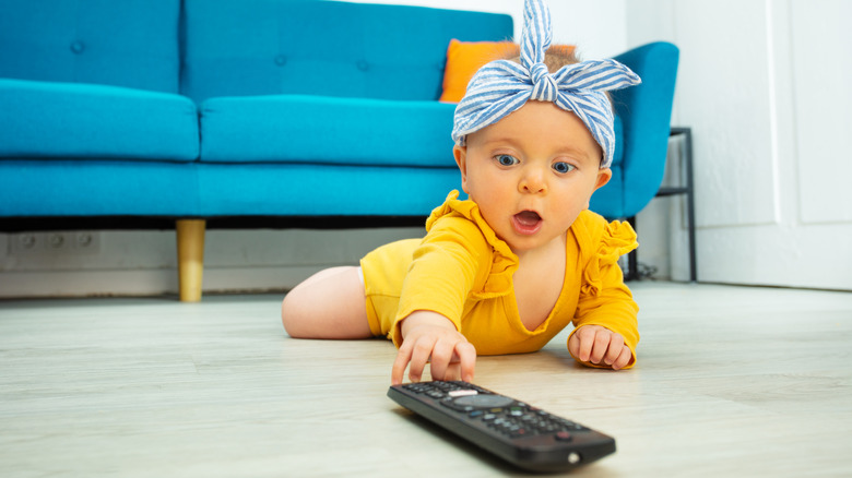 A baby with blue eyes touching a TV remote