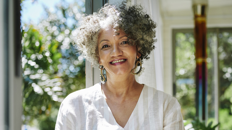 A woman with a curly gray bob wearing a white top and statement earrings.